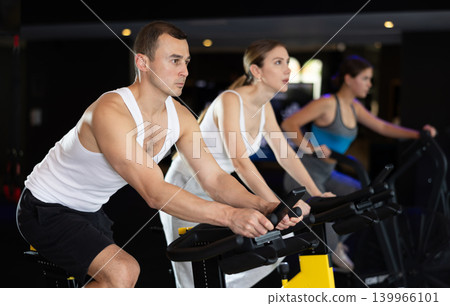 Sportive young guy doing spin bike exercises in well-equipped gym Sportive young guy doing spin bike exercises in well-equipped gym 139966101