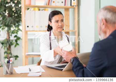 Adult female doctor giving prescribed medication to elderly male patient Adult female doctor giving prescribed medication to elderly male patient 139966136