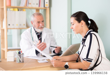 Woman explains her complaints to an elderly male doctor sitting in front of laptop Woman explains her complaints to an elderly male doctor sitting in front of laptop 139966138