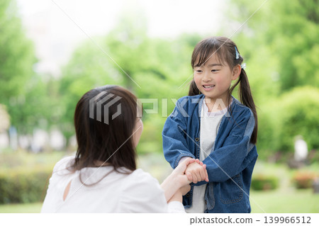 An image of a parent-child lifestyle: smiling, holding hands, gazing into each other's eyes, and touching each other amidst the fresh greenery of nature. 139966512