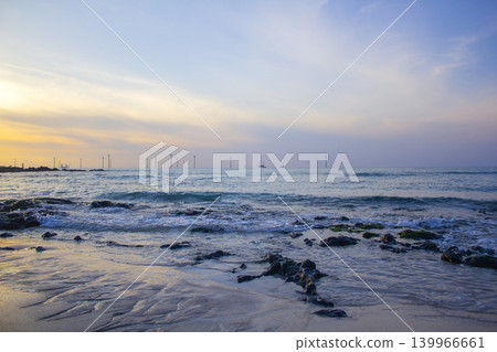 It is a beach scene with the sun setting. 139966661