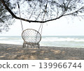 A woven rope hammock hangs under a pine tree on the beach by the sea. 139966744