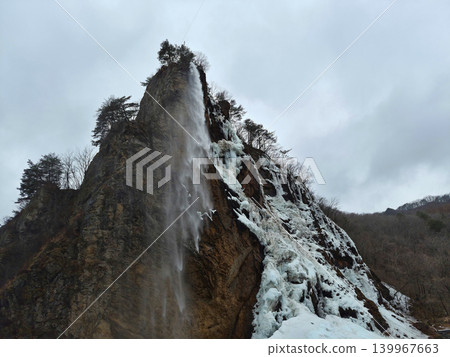 It is a winter cliff with a flowing waterfall. 139967663