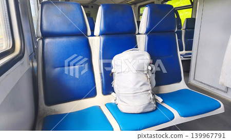 A gray backpack on blue seats inside a commuter train car during a daytime commute. Urban transportation, car interior in Ukraine. Train ride 139967791