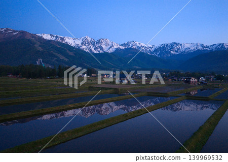 The snow-capped peaks of the Hakuba Three Peaks are reflected in the water of a rice paddy in the early morning, in Hakuba Village, Nagano Prefecture (aerial photograph taken by drone). The snow-capped peaks of the Hakuba Three Peaks are reflected in the water of a rice paddy in the early morning, in Hakuba Village, Nagano Prefecture (aerial photograph taken by drone). 139969532