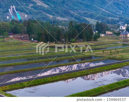 The snow-capped Hakuba mountain range reflected in the water of a rice paddy in the early morning, Hakuba Village, Nagano Prefecture (aerial photograph taken by drone). The snow-capped Hakuba mountain range reflected in the water of a rice paddy in the early morning, Hakuba Village, Nagano Prefecture (aerial photograph taken by drone). 139969537