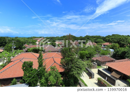 [Okinawa Prefecture] A cluster of red-tiled roof houses on Taketomi Island under a clear blue sky 139970016