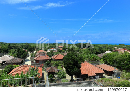 [Okinawa Prefecture] A cluster of red-tiled roof houses on Taketomi Island under a clear blue sky 139970017