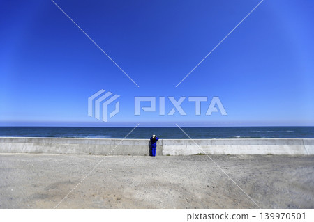 A woman gazes at the sea from the seawall, against a backdrop of blue sky and the horizon. 139970501