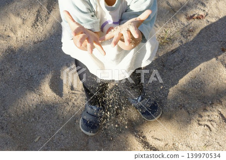 A child playing in the park's sandbox, letting sand fall from their hands. A child playing in the park's sandbox, letting sand fall from their hands. 139970534