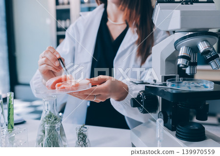 Scientists in lab coats work with plants in a modern lab, focusing on research and experimentation under bright, sterile conditions. 139970559