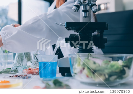 Scientists in lab coats work with plants in a modern lab, focusing on research and experimentation under bright, sterile conditions. Scientists in lab coats work with plants in a modern lab, focusing on research and experimentation under bright, sterile conditions. 139970560