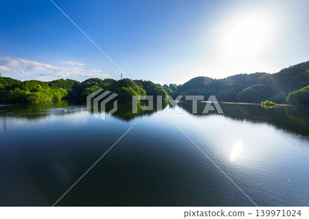 Early summer at Nunome Dam: The blue sky and path of light reflected on the surface of the lake, which is filled to the brim. (25) 139971024