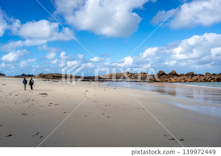 Walkers crossing Coz Pors beach toward granite reef in Brittany, France Walkers crossing Coz Pors beach toward granite reef in Brittany, France 139972449