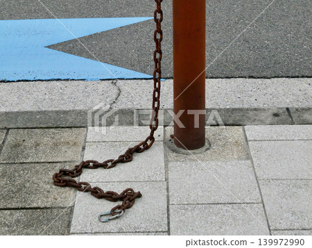 A brown bollard and a rusty chain are installed on the side of the road. A brown bollard and a rusty chain are installed on the side of the road. 139972990