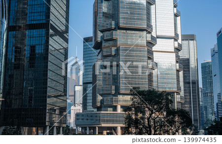 Unique modern octagonal glass facade skyscraper dominates dense corporate business financial district standing proudly under bright blue daytime sky alongside multiple office towers 139974435