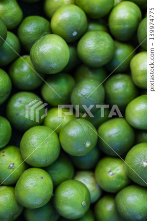 Fresh Harvested Green Limes For Sale At A Farmer Market. Close up of ripe citrus fruits with textured skin on local grocery stall, ideal for refreshing beverages or healthy cooking themes. Fresh Harvested Green Limes For Sale At A Farmer Market. Close up of ripe citrus fruits with textured skin on local grocery stall, ideal for refreshing beverages or healthy cooking themes. 139974775