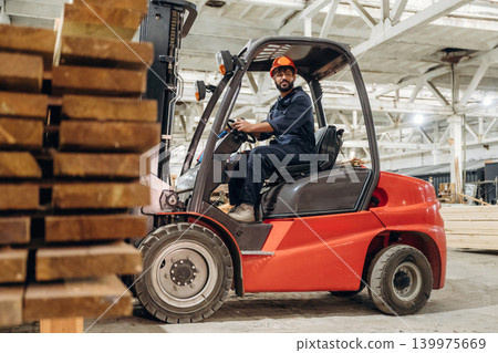 Warehouse worker operating a forklift while handling wooden materials 139975669