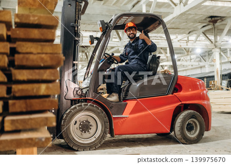 Warehouse worker operating a forklift while handling wooden materials Warehouse worker operating a forklift while handling wooden materials 139975670
