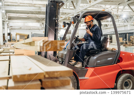 Warehouse worker operating a forklift while handling wooden materials 139975671