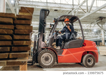 Heavy material, lifting the planks. Warehouse worker operating a forklift while handling wooden materials 139975675