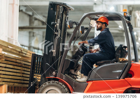 Lifting bunch of planks. Warehouse worker operating a forklift while handling wooden materials Lifting bunch of planks. Warehouse worker operating a forklift while handling wooden materials 139975706