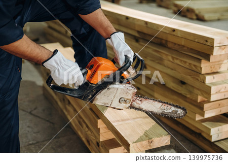 Using a chainsaw. Close-up of a carpenter working with wood using professional tools in a workshop 139975736