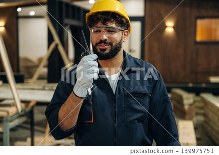 Talking by walkie talkie. Portrait of a male carpenter posing in a woodworking workshop Talking by walkie talkie. Portrait of a male carpenter posing in a woodworking workshop 139975751