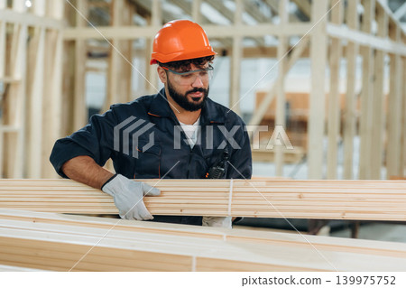 Moving the planks, walking. Male carpenter working with wooden materials in a professional workshop Moving the planks, walking. Male carpenter working with wooden materials in a professional workshop 139975752