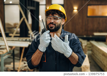 Talking by walkie talkie. Portrait of a male carpenter posing in a woodworking workshop 139975753