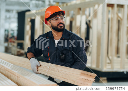 Moving the planks, walking. Male carpenter working with wooden materials in a professional workshop Moving the planks, walking. Male carpenter working with wooden materials in a professional workshop 139975754