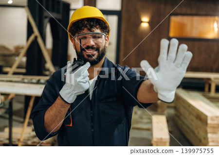 Talking by walkie talkie. Portrait of a male carpenter posing in a woodworking workshop 139975755