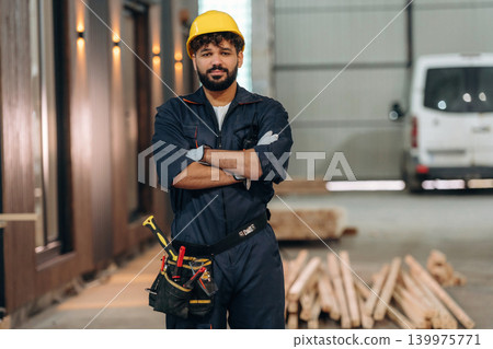 Arms crossed, standing. Portrait of a male carpenter posing in a woodworking workshop Arms crossed, standing. Portrait of a male carpenter posing in a woodworking workshop 139975771