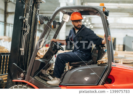 Driving, skilled employee. Warehouse worker operating a forklift while handling wooden materials Driving, skilled employee. Warehouse worker operating a forklift while handling wooden materials 139975783