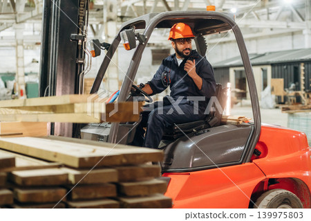 Ready to load. Warehouse worker operating a forklift while handling wooden materials Ready to load. Warehouse worker operating a forklift while handling wooden materials 139975803