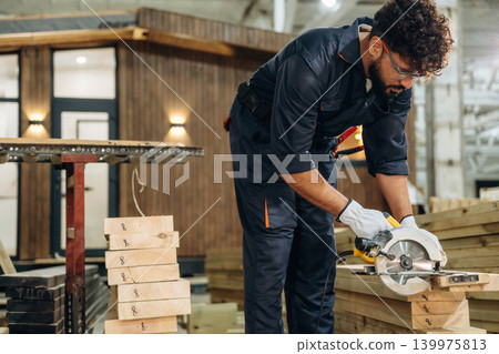 View from the side, cutting the wood. Male carpenter working with materials in a professional workshop View from the side, cutting the wood. Male carpenter working with materials in a professional workshop 139975813