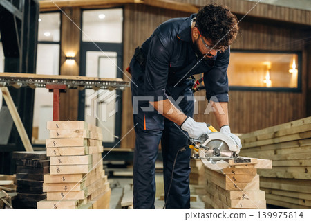View from the side, cutting the wood. Male carpenter working with materials in a professional workshop View from the side, cutting the wood. Male carpenter working with materials in a professional workshop 139975814