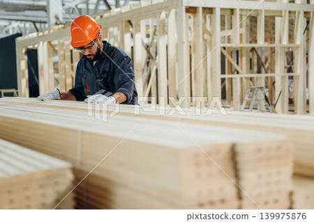Bunch of new planks. Male carpenter working with wooden materials in a professional workshop Bunch of new planks. Male carpenter working with wooden materials in a professional workshop 139975876