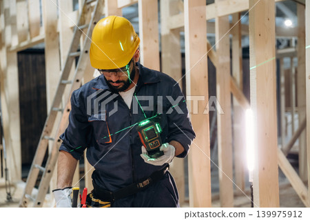 Leveler device is in hands. Male carpenter working with wooden materials in a professional workshop Leveler device is in hands. Male carpenter working with wooden materials in a professional workshop 139975912
