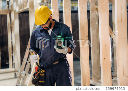 Leveler device is in hands. Male carpenter working with wooden materials in a professional workshop Leveler device is in hands. Male carpenter working with wooden materials in a professional workshop 139975913