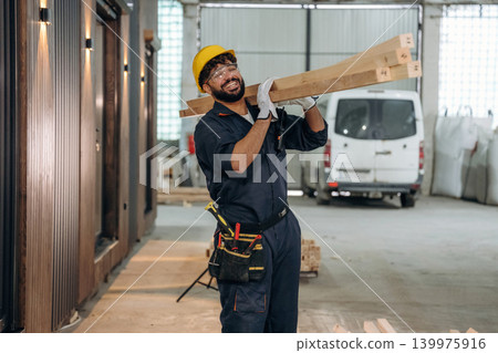 Plank is in hands, moving it. Male carpenter working with wooden materials in a professional workshop Plank is in hands, moving it. Male carpenter working with wooden materials in a professional workshop 139975916