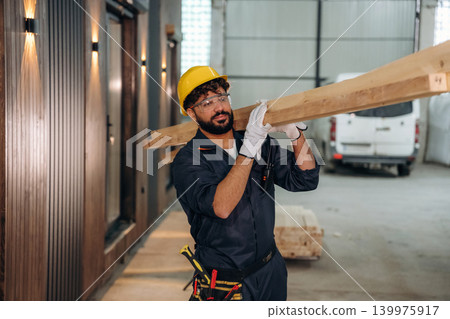 Construction of the house, walking and moving the planks. Male carpenter working with wooden materials in a professional workshop Construction of the house, walking and moving the planks. Male carpenter working with wooden materials in a professional workshop 139975917