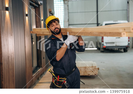 Construction of the house, walking and moving the planks. Male carpenter working with wooden materials in a professional workshop Construction of the house, walking and moving the planks. Male carpenter working with wooden materials in a professional workshop 139975918