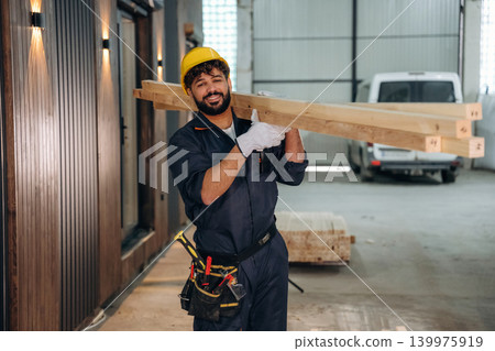 Construction of the house, walking and moving the planks. Male carpenter working with wooden materials in a professional workshop Construction of the house, walking and moving the planks. Male carpenter working with wooden materials in a professional workshop 139975919