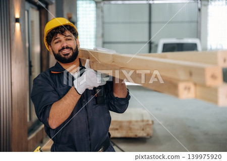 Construction of the house, walking and moving the planks. Male carpenter working with wooden materials in a professional workshop Construction of the house, walking and moving the planks. Male carpenter working with wooden materials in a professional workshop 139975920