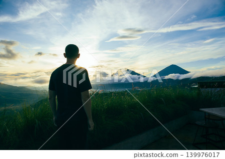 Person watches sunset over mountains and clouds in Bali Person watches sunset over mountains and clouds in Bali 139976017
