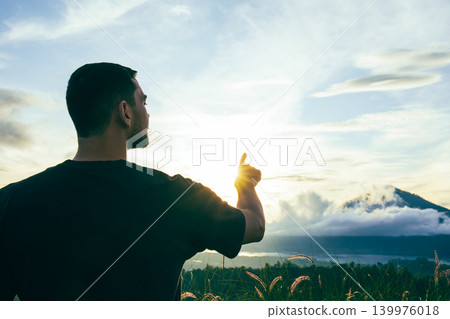 Man gestures towards sunrise in Kintamani Bali with mountains Man gestures towards sunrise in Kintamani Bali with mountains 139976018