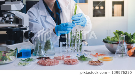 Scientists in lab coats work with plants in a modern lab, focusing on research and experimentation under bright, sterile conditions. Scientists in lab coats work with plants in a modern lab, focusing on research and experimentation under bright, sterile conditions. 139976250