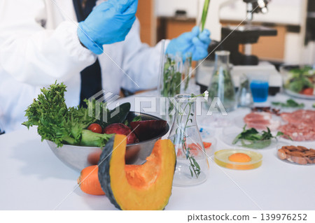 Scientists in lab coats work with plants in a modern lab, focusing on research and experimentation under bright, sterile conditions. 139976252