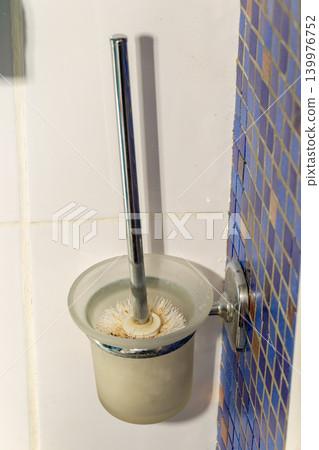 Toilet Brush in Holder Mounted on Tiled Bathroom Wall With Worn Bristles and Stains Toilet Brush in Holder Mounted on Tiled Bathroom Wall With Worn Bristles and Stains 139976752
